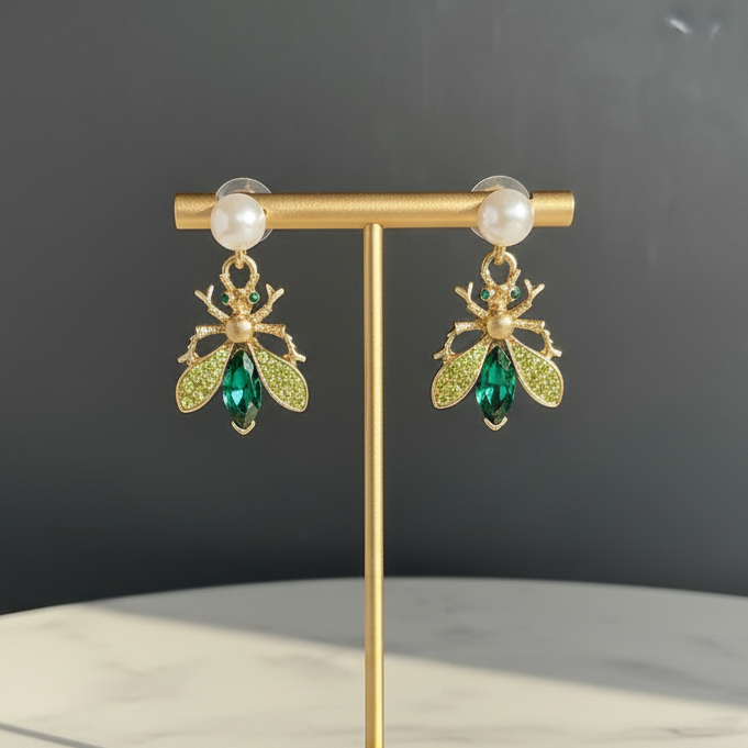 Gold earring stand with green and gold bee-shaped earrings on a marble surface.